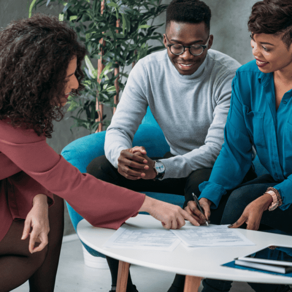 financial planning session between female financial advisor and a male and female client signing a document